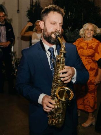 A man in a stylish suit sets the tone with his melodic trumpet playing, as everyone joyfully dances and celebrates, creating a vibrant and lively atmosphere at the wedding